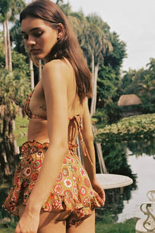 Woman wearing a short floral print dress with red, orange, and yellow flowers, halter neckline, shown from the side.
