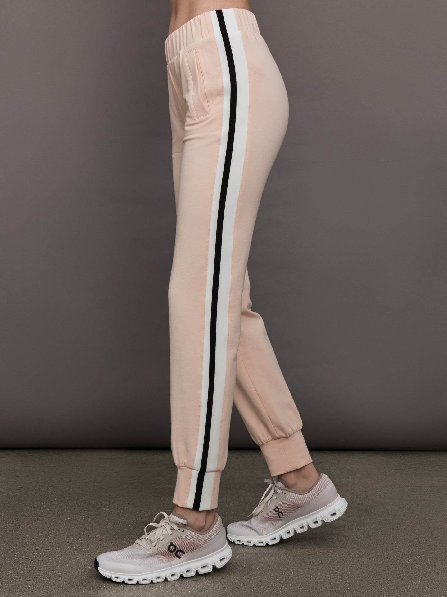Model wears baby pink jogger pants with side stripes, elastic waistband, and cuffed ankles.
