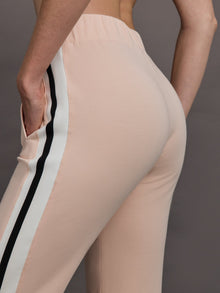 Model wears baby pink jogger pants with side stripes, elastic waistband, and cuffed ankles.

