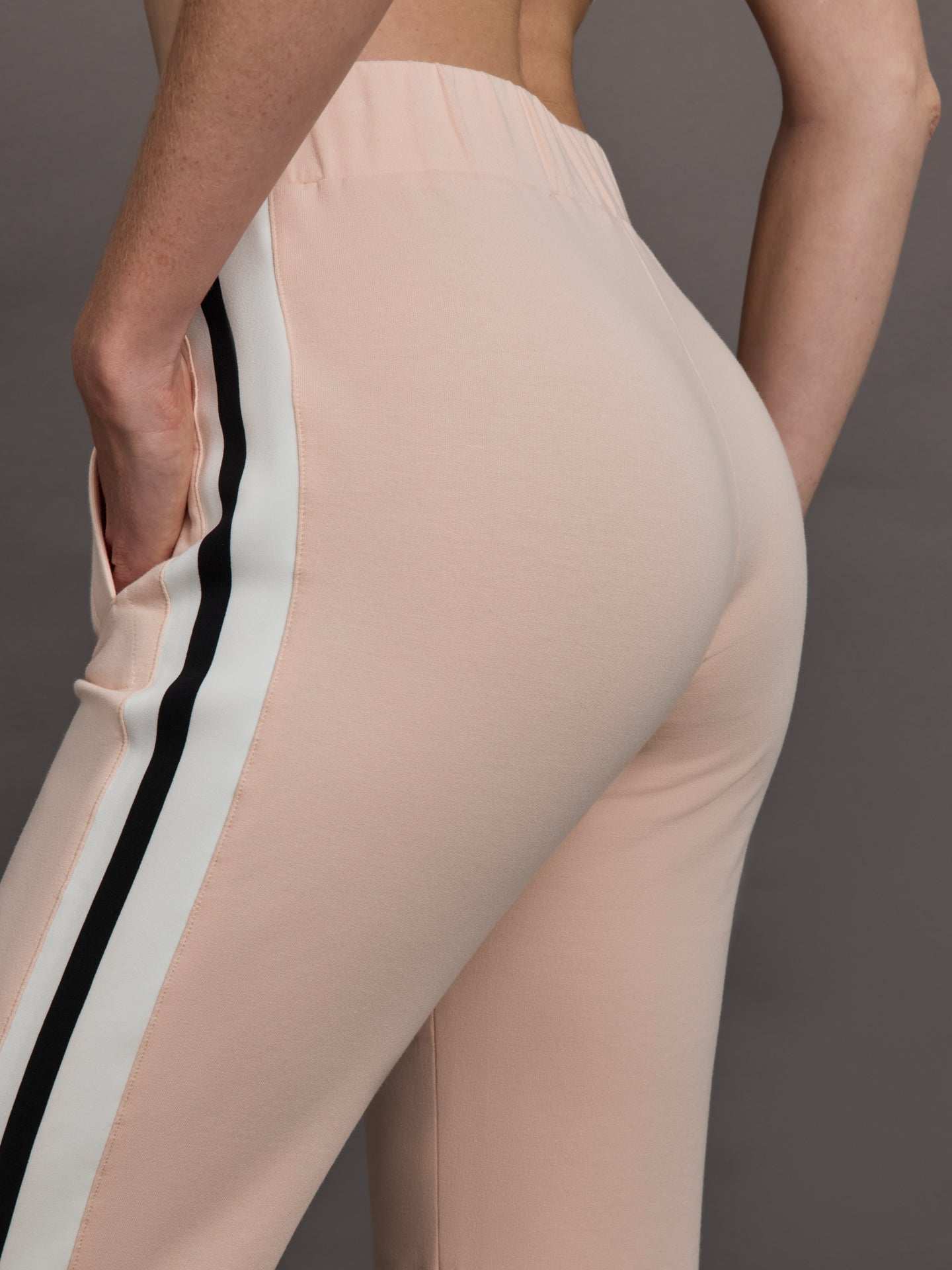 Model wears baby pink jogger pants with side stripes, elastic waistband, and cuffed ankles.
