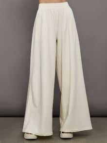 Model wears a pair of oversized wide leg cream colored sweatpants. 