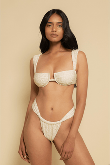 Oat textured bikini bottom with curved waistband and textured fabric detail on model against neutral background.