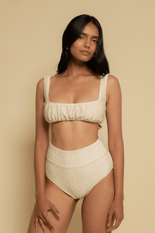 Cream textured crop top with square neckline and thick shoulder straps on model against neutral background.