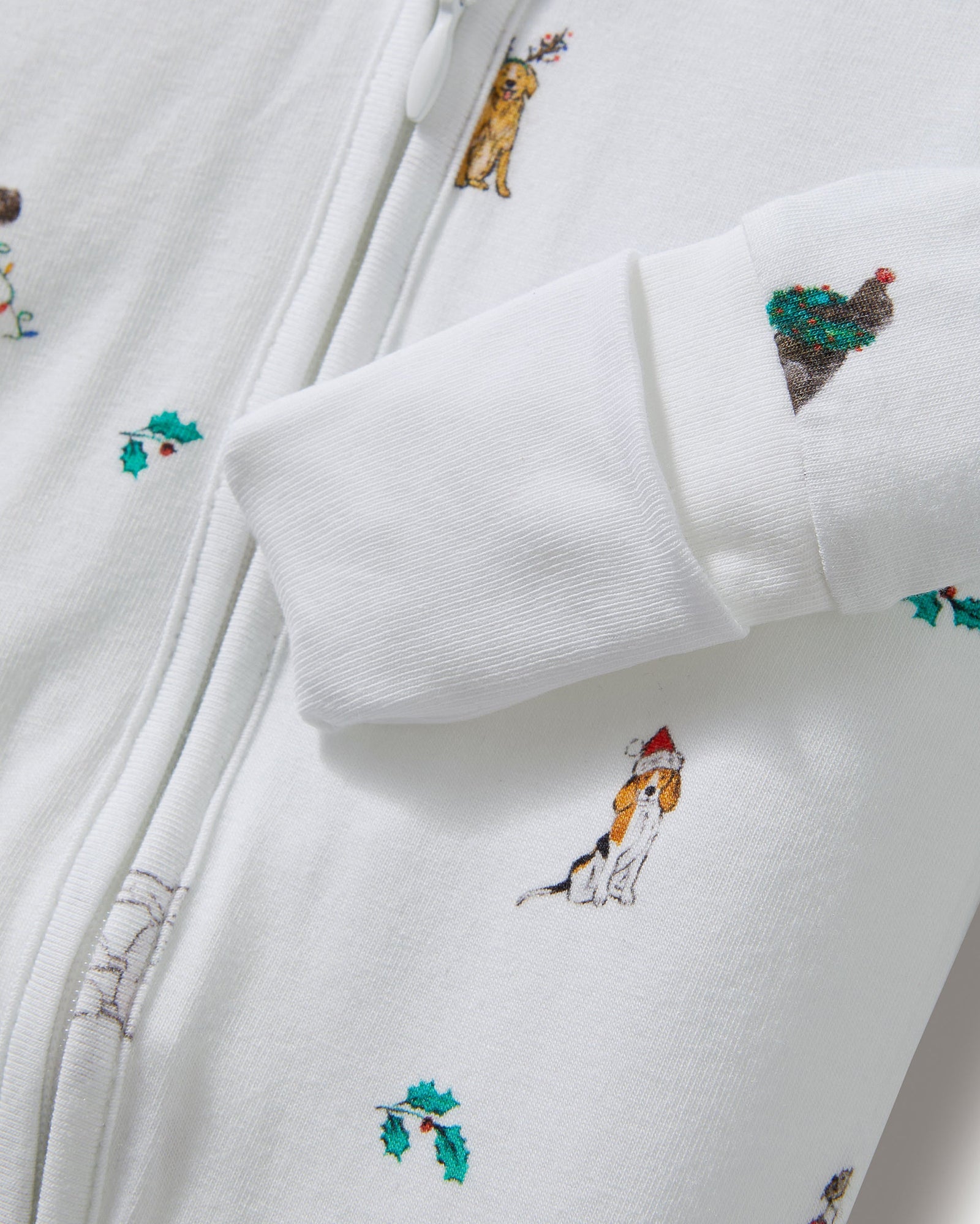 The Baby's Pima Peekaboo Romper in Jingle Paws is a white, long-sleeve onesie with a front zipper, decorated with colorful dogs and green bones. The left leg appears slightly folded over.
