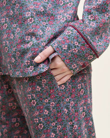 The Women's Pima Pajama Set in Fleurs de Saison features long sleeves and a small floral print in pink, white, and blue on gray. The set includes a button-up top with a chest pocket and matching pants.