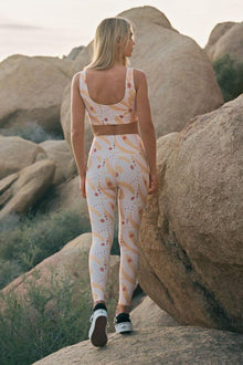Woman wearing white leggings with yellow and red palm leaf print and matching crop top.
