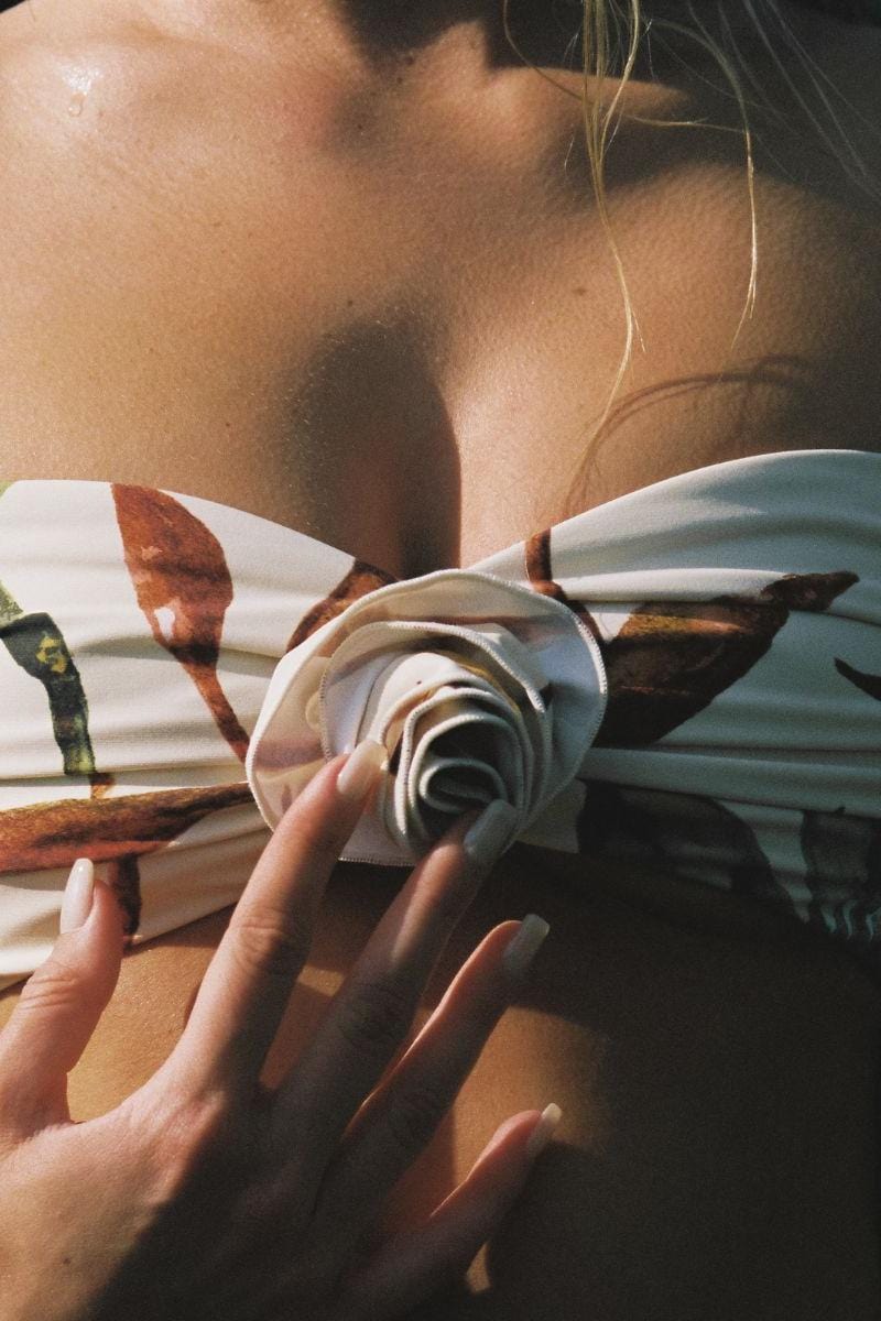 White bandeau bikini top with rust and brown floral pattern, worn by person holding rolled fabric swatches.