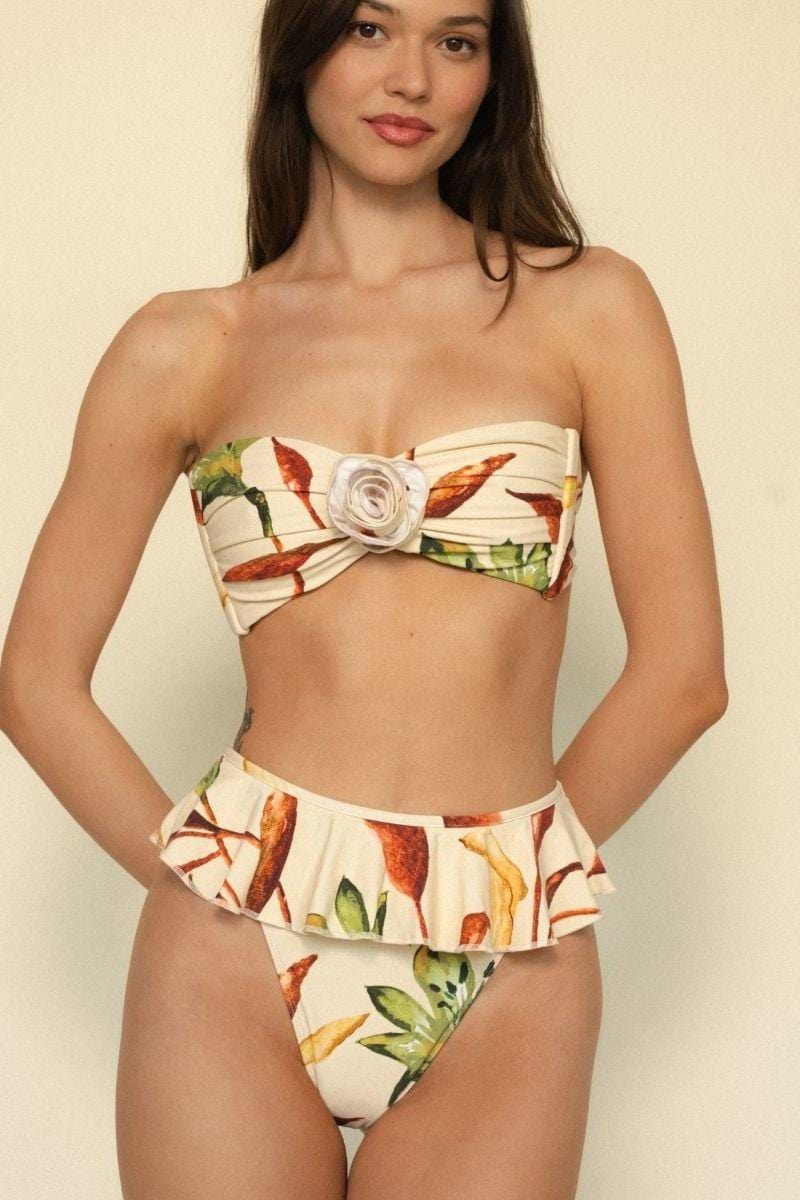 Cream bandeau bikini top with red and green floral print, white center bow detail, worn on model against neutral background.