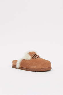 Tan suede slide with cream shearling lining and decorative buckle detail on upper.