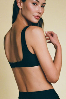 Black racerback bikini top with minimal back coverage on model against neutral background.