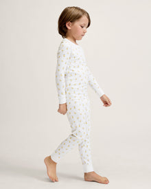 A young child with light brown hair stands barefoot on a plain background, wearing the Kid's Pima Snug Fit Pajama Set in Tres Chick and looking slightly to the side.