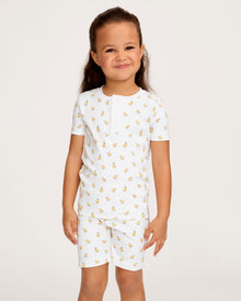 A young child with long brown hair smiles while wearing the Kid's Pima Snug Fit Short Set in Tres Chick, standing against a plain light background.