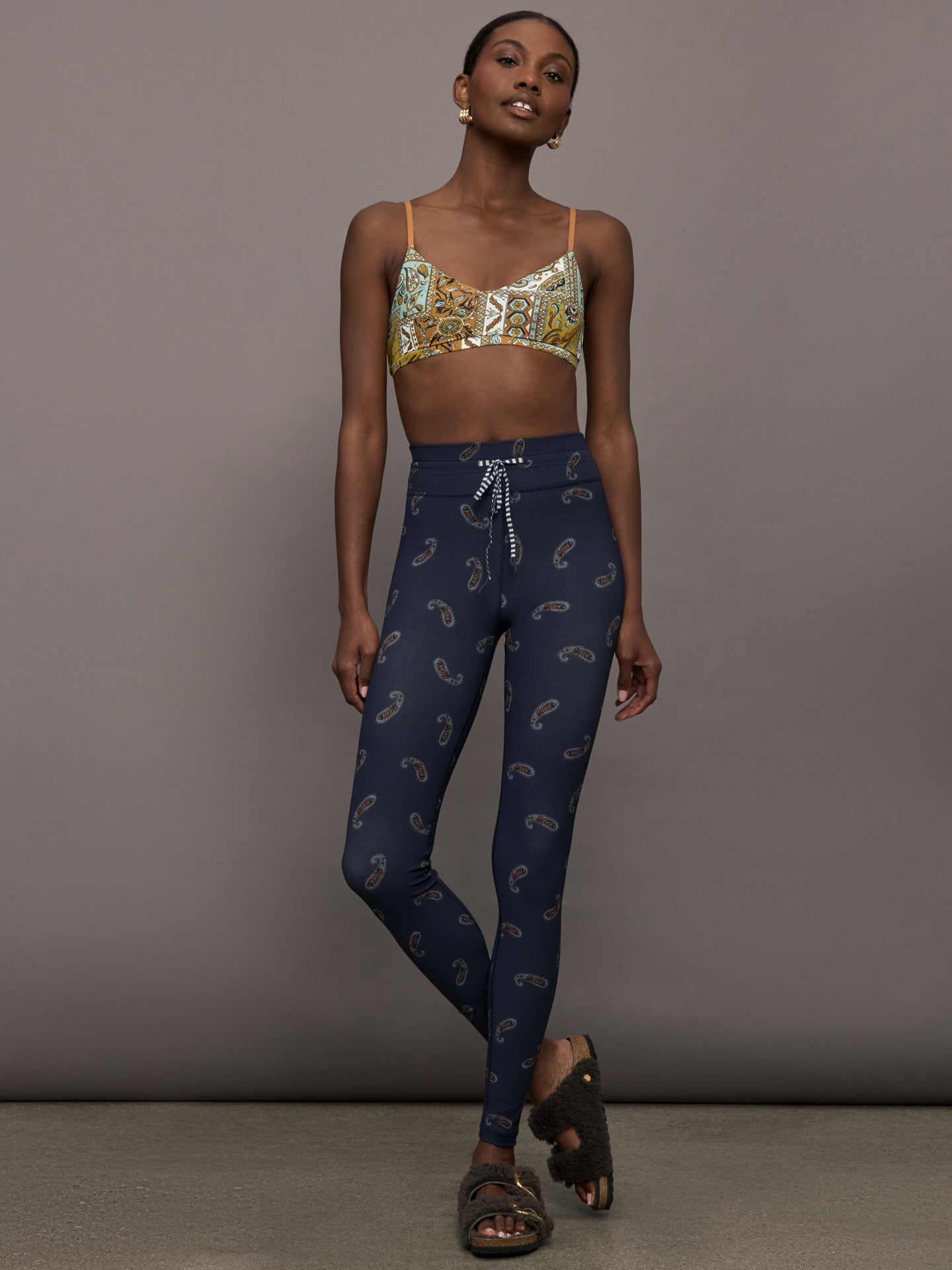 Model is wearing a paisley v neck sports bra with brown, white, and blue coloring. 