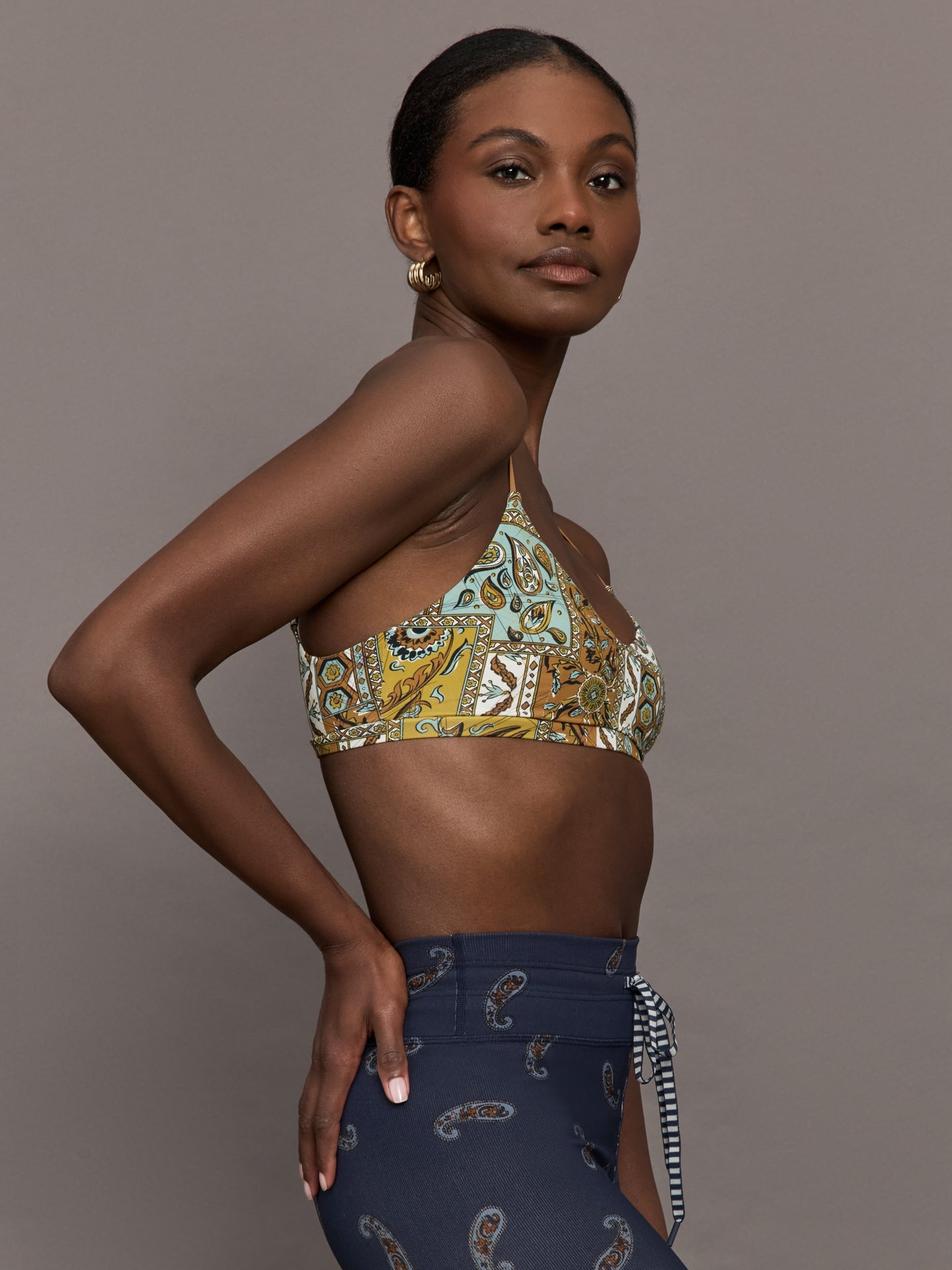 Model is wearing a paisley v neck sports bra with brown, white, and blue coloring. 