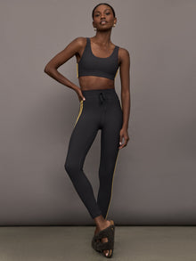 Model is wearing a black scoopneck sports bra with yellow striped sides. 