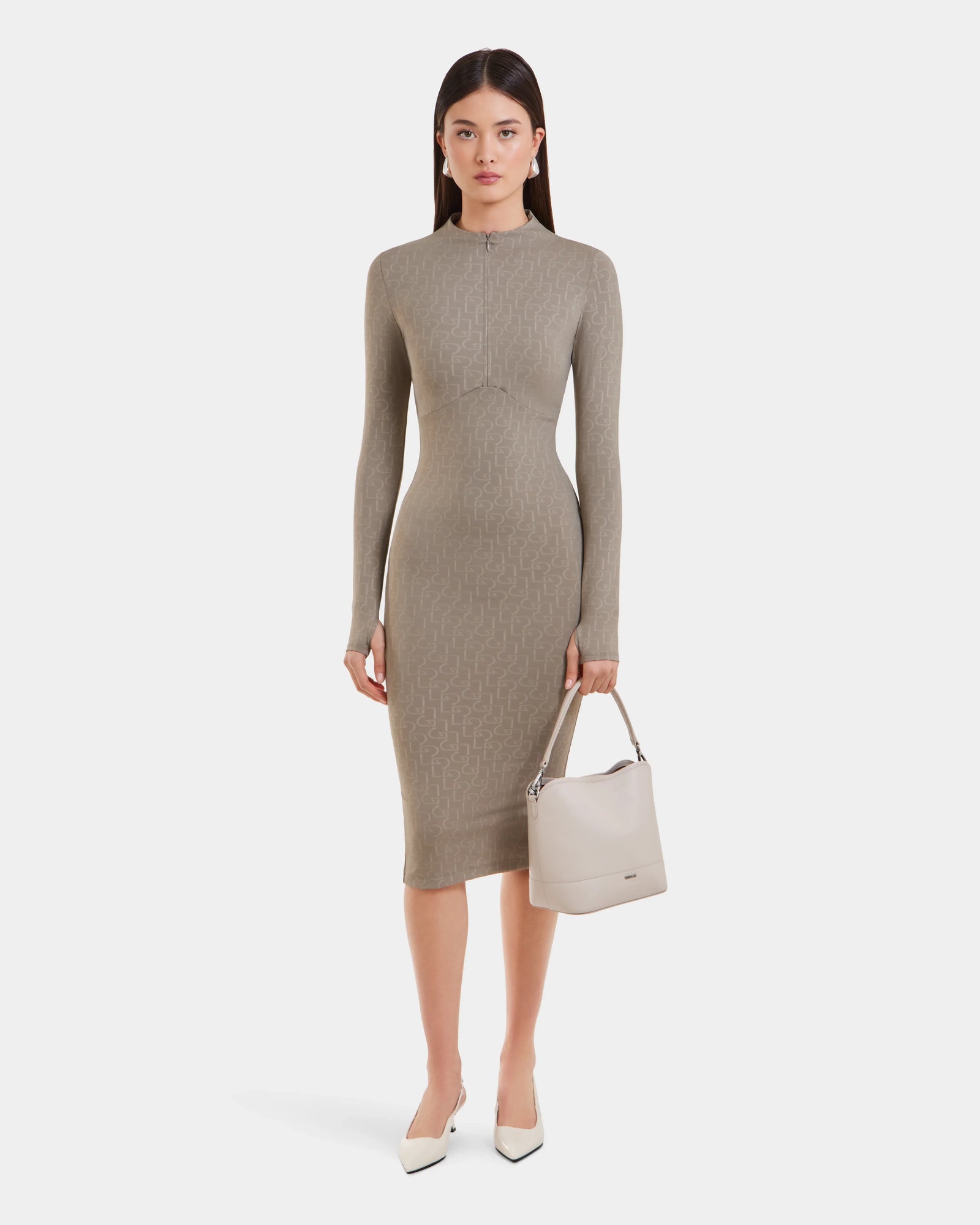 A woman stands against a white background wearing the Rudsak MAYLIN - 8523504 Cement Pattern women’s long fitted dress, paired with white pointed-toe heels and holding a beige handbag in her left hand.