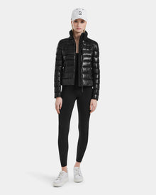 A woman wears the MELISSA - 8121000 BLACK puffer jacket with black leggings, white sneakers, and a white baseball cap, standing facing forward against a plain light background.