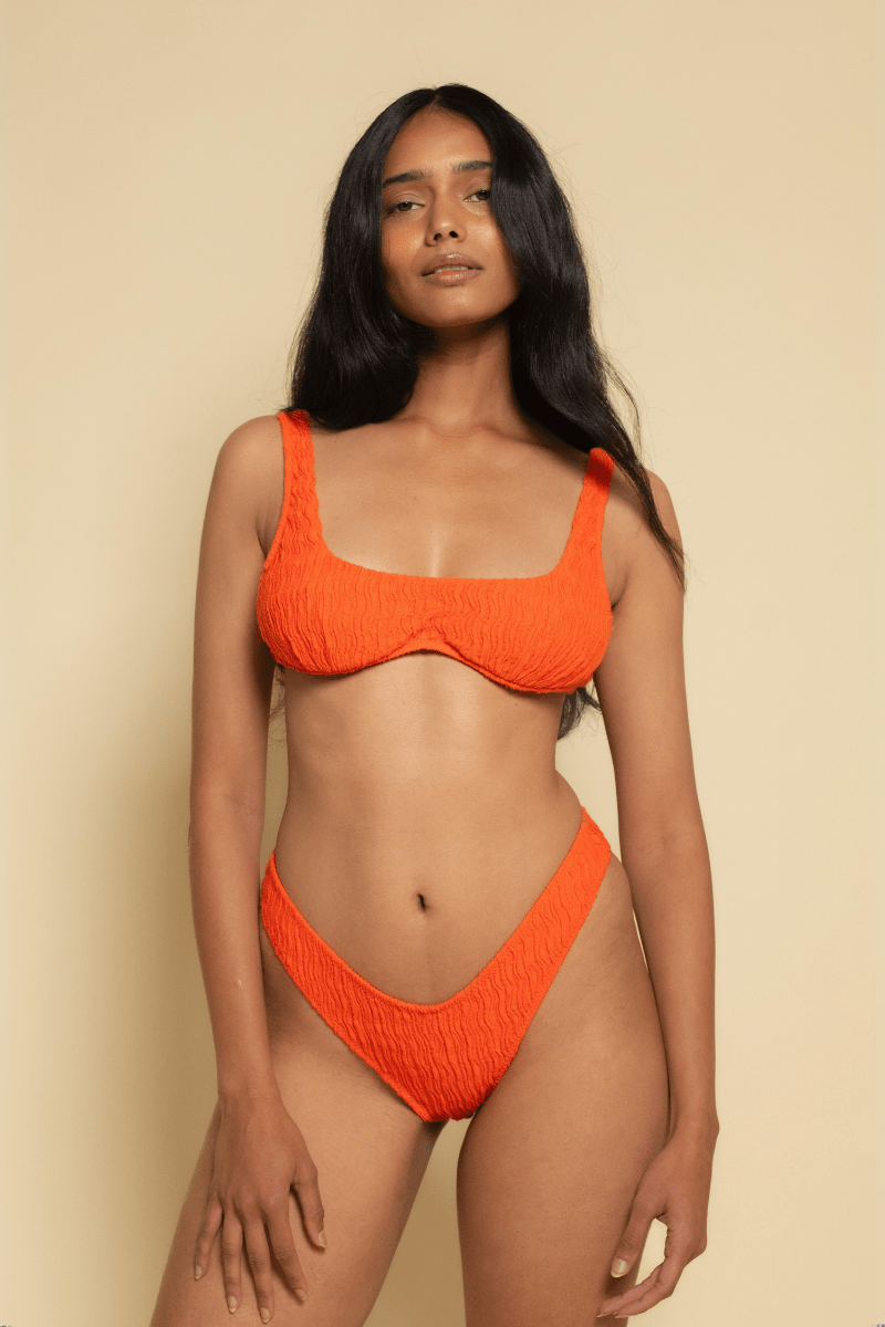 Tangerine bikini top with textured fabric and wide shoulder straps on a model against a neutral background.