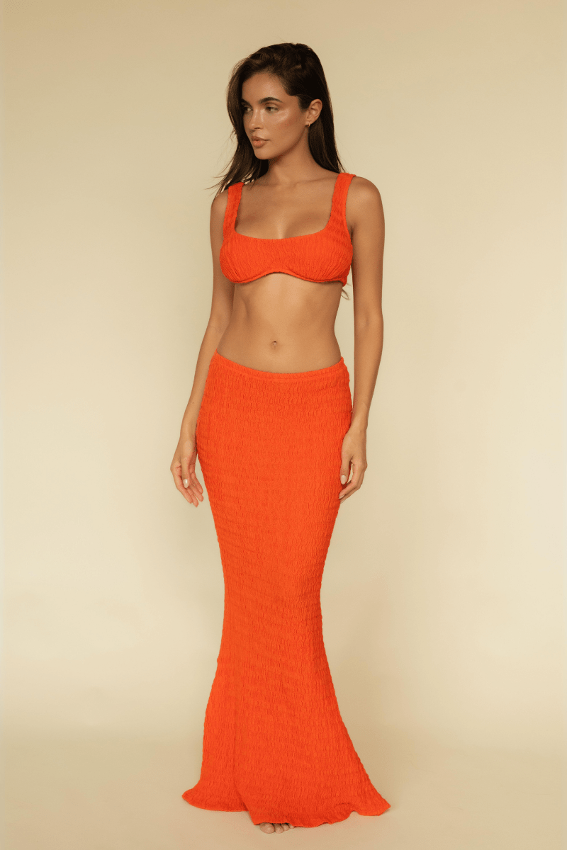 Woman wearing a tangerine ribbed two-piece set with a square-neckline bikini top and floor-length maxi skirt.