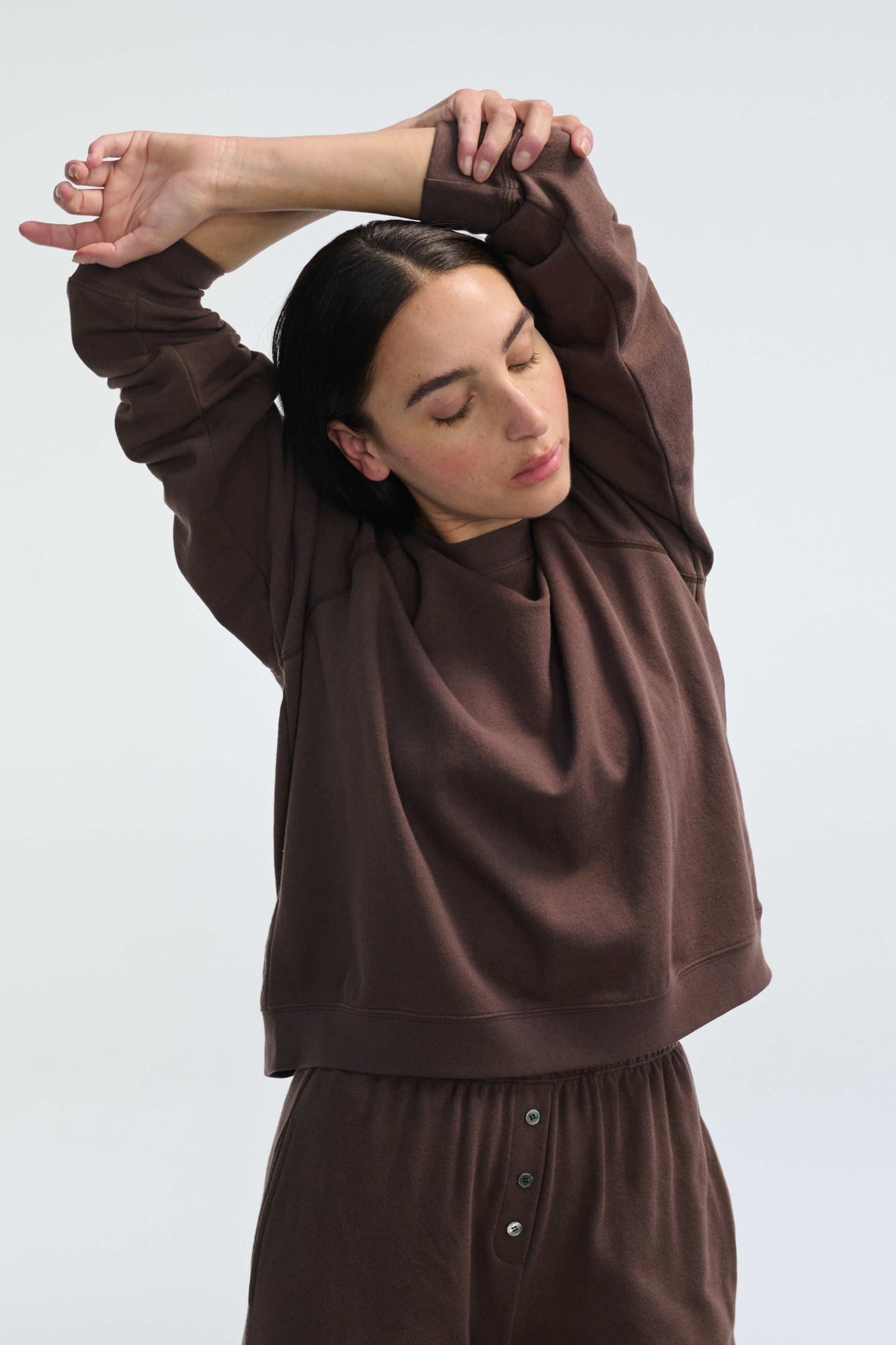 Woman wearing a brown outfit with long sleeves and pants against a white background