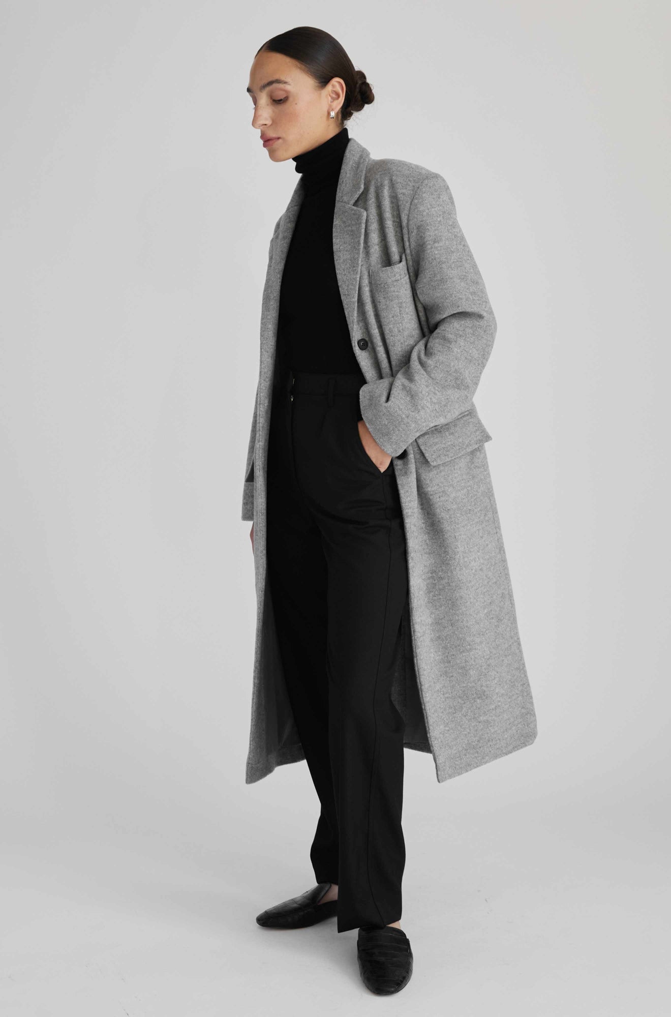 Person wearing a gray coat over a black outfit on a light gray background