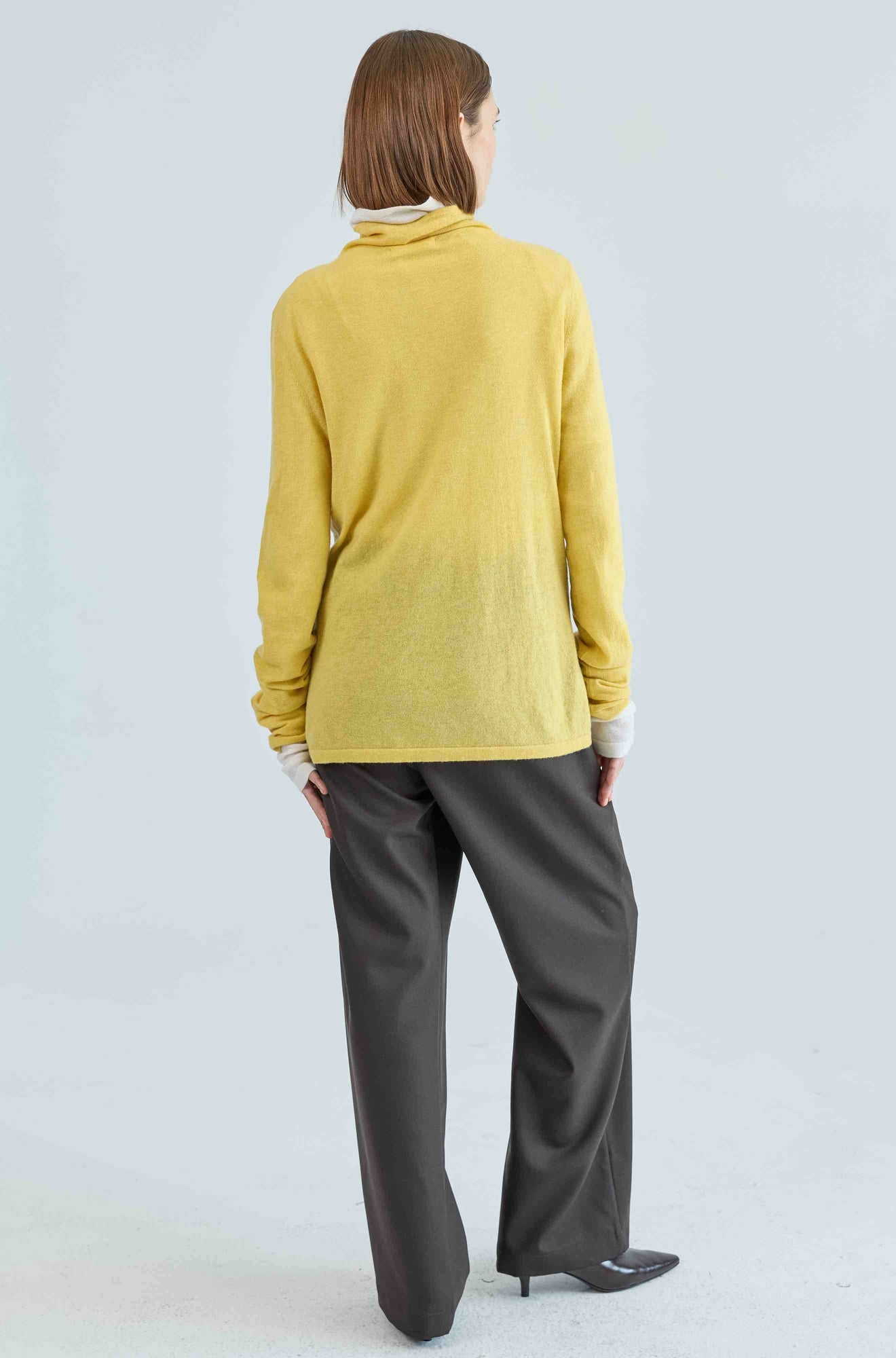 Person wearing a yellow sweater and brown pants on a light gray background