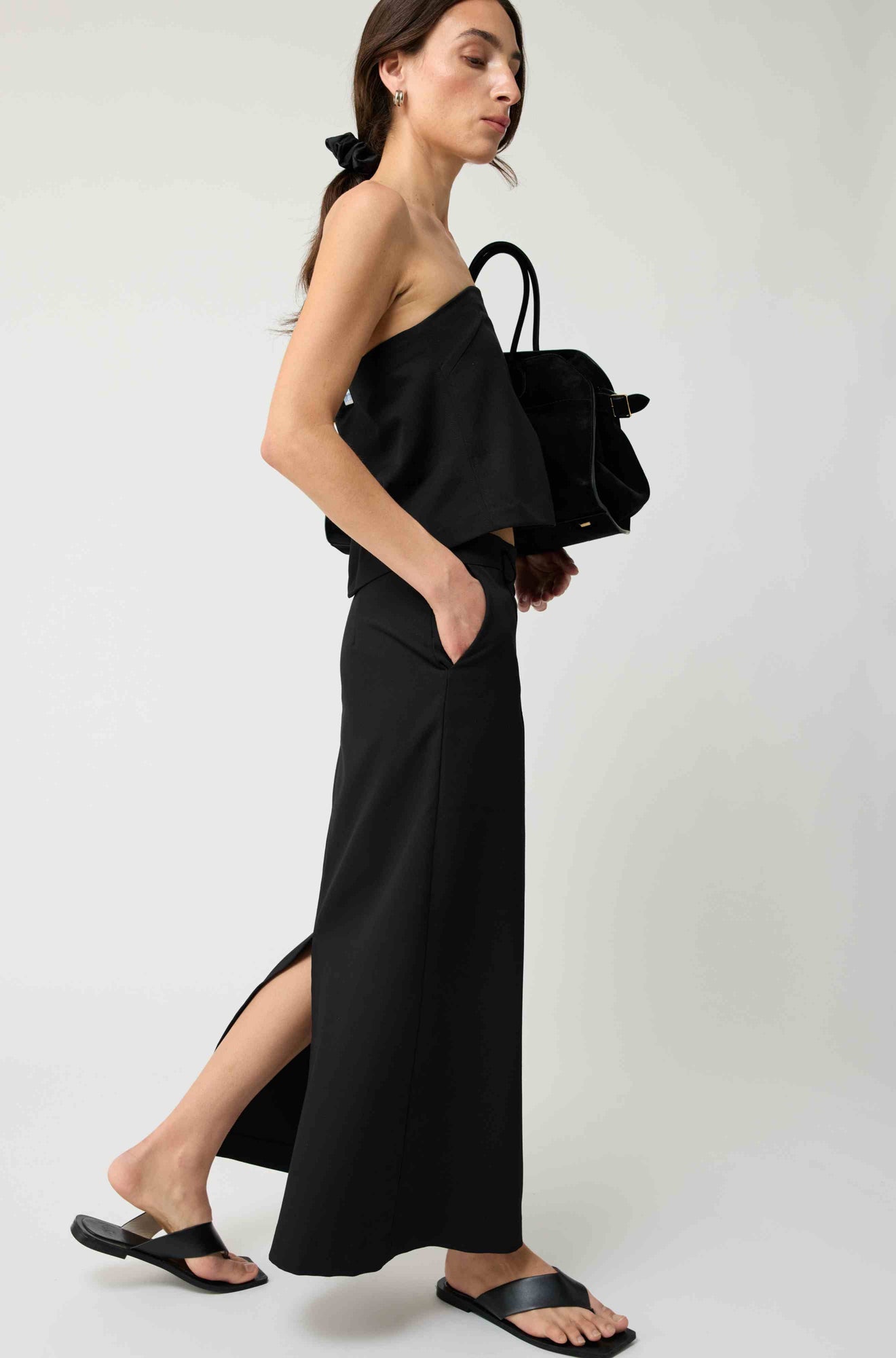 Woman wearing a black strapless top with a matching black skirt on a light grey background
