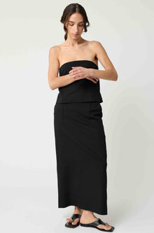 Woman wearing a black strapless top with a matching black skirt on a light grey background