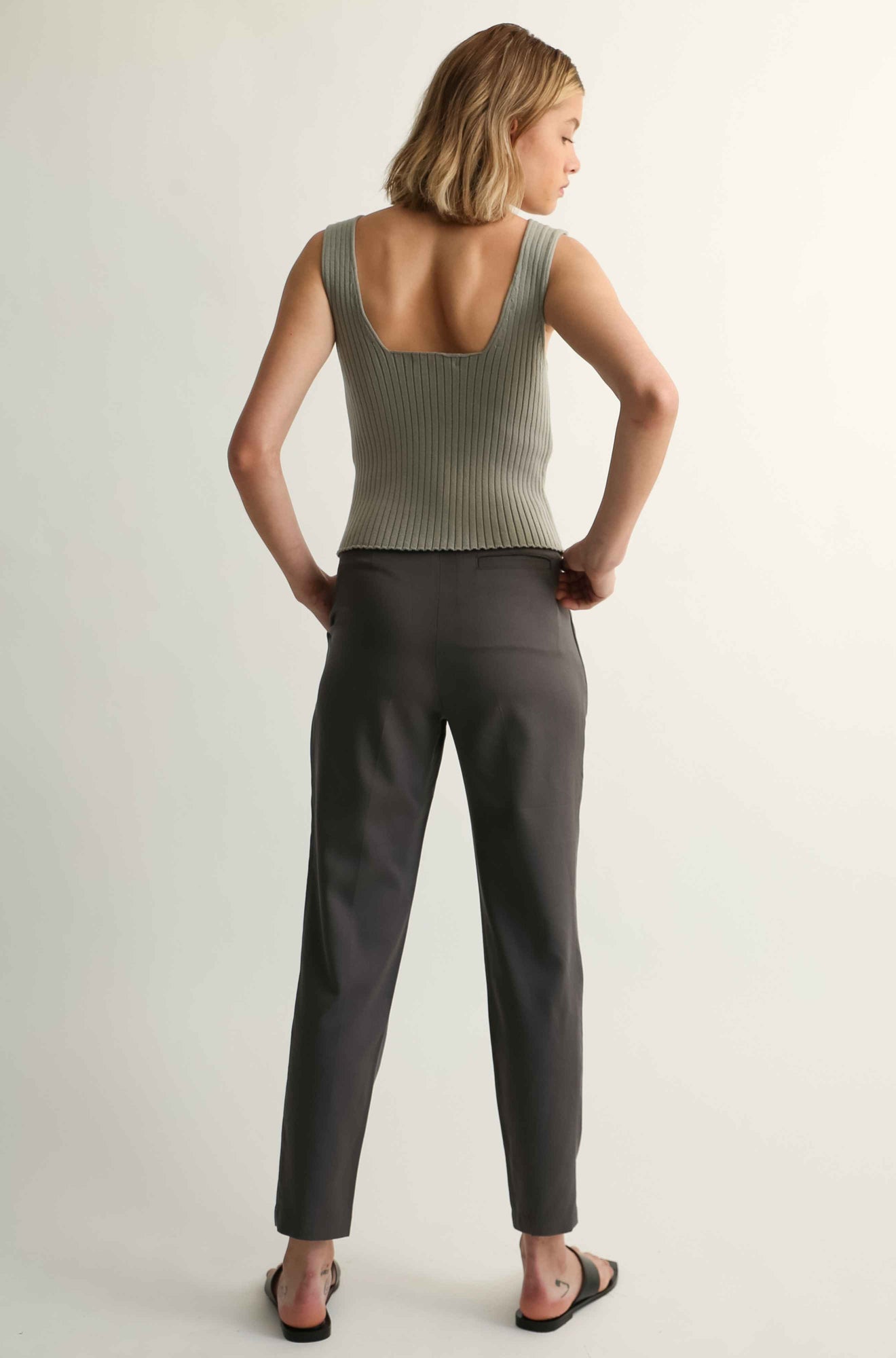 Woman wearing a green tank top and gray pants on a plain background