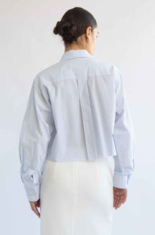 Person wearing a light blue striped shirt and white pants against a plain background
