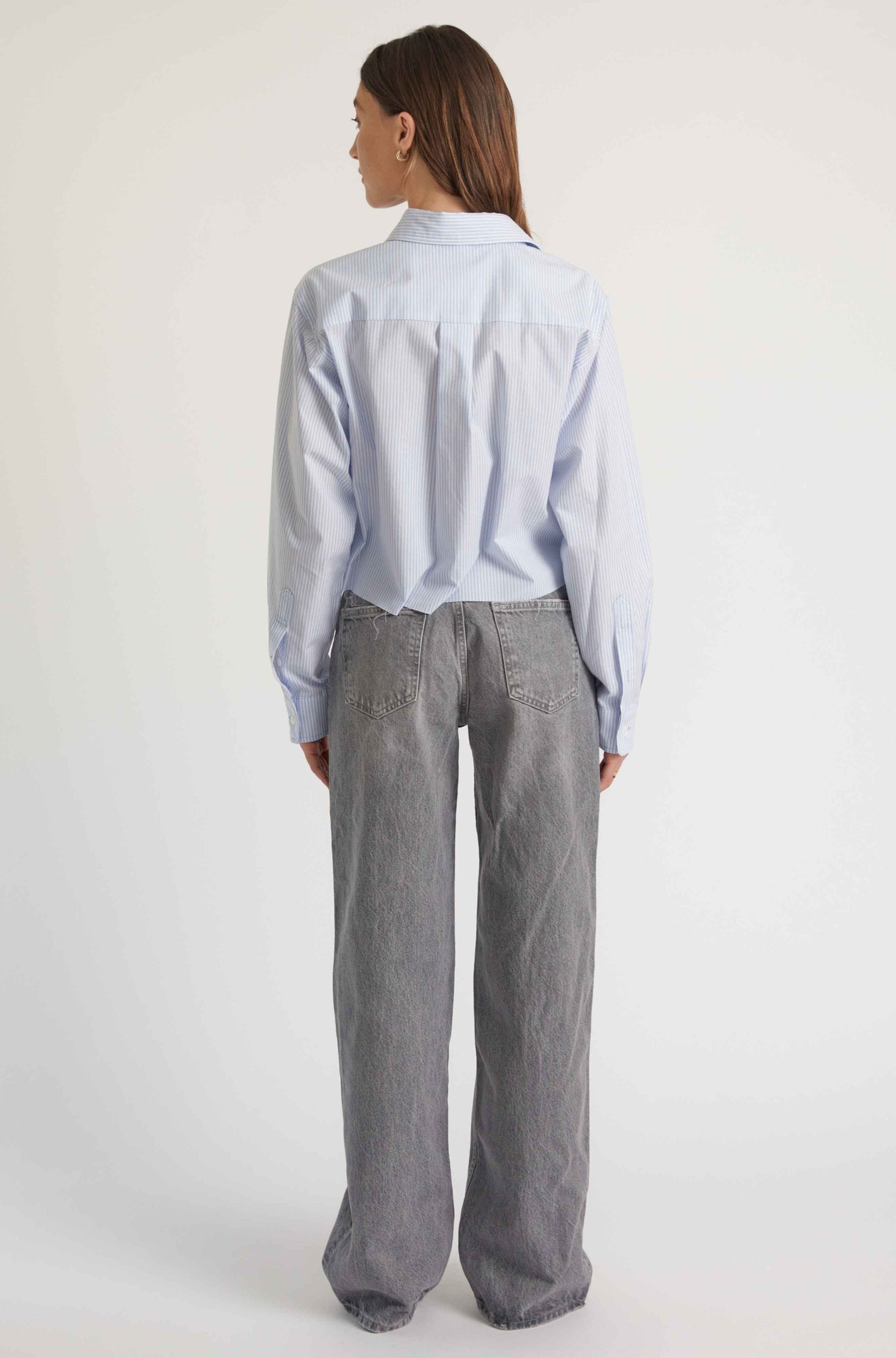 Person wearing a light blue shirt and gray pants on a white background