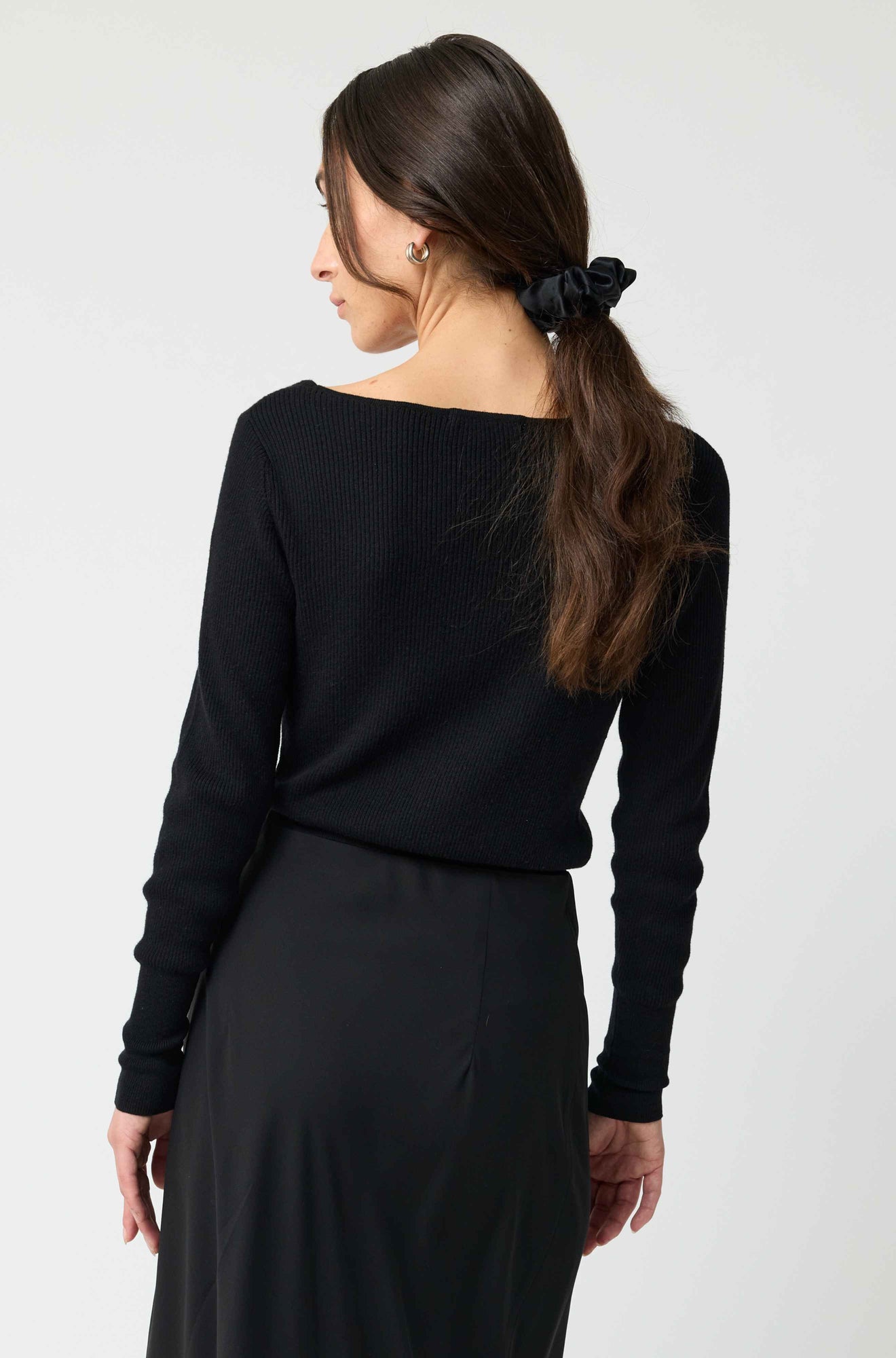 Woman wearing a black long-sleeve top and black skirt against a white background