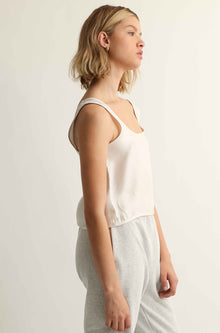 Woman wearing a white sleeveless top and light gray pants against a plain background