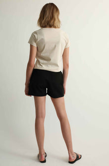 Person wearing a beige t-shirt and black shorts on a plain background