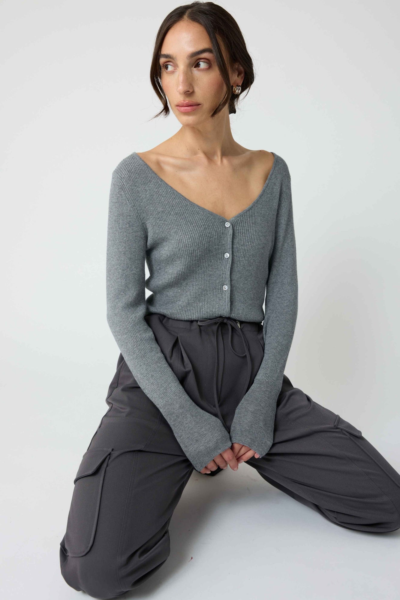 Woman wearing a grey cardigan with grey cargo pants on a light grey background