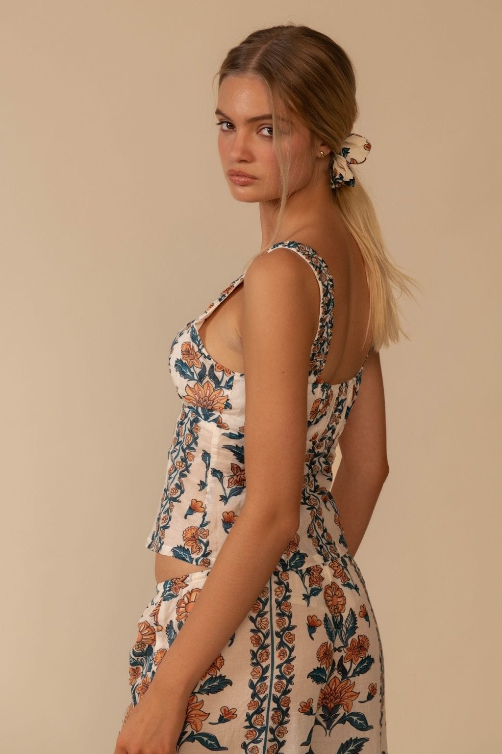 Sleeveless tank top with orange and navy floral print on cream background, scoop neckline, fitted silhouette.