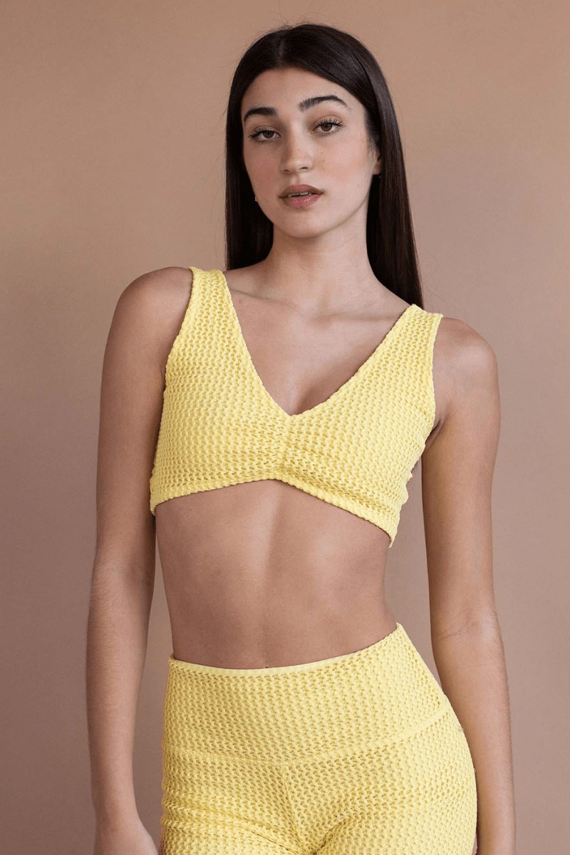 Yellow crochet bikini top with V-neckline and textured knit fabric, displayed on model against neutral background.