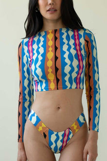 Bikini bottom with blue, yellow, pink, and orange abstract geometric wave pattern on cream background.