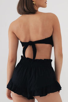 Black shorts with smocked waistband, cutout back detail, and ruffled hem.