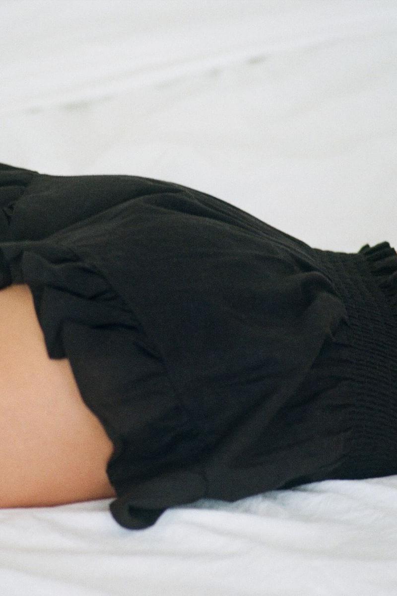 Black shorts with ruffled leg cuffs and elastic waistband, displayed on a model.