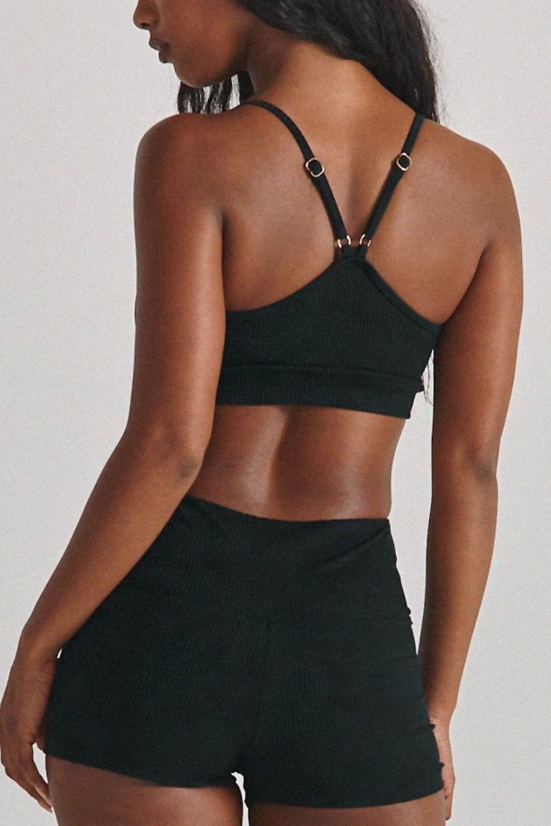 Black ribbed crop top and micro shorts set worn by model, shown from back view.