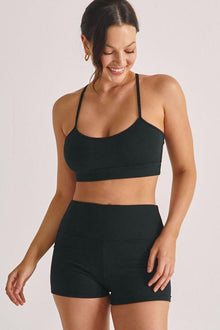 Woman wearing black ribbed crop top and matching micro bike shorts against neutral background.
