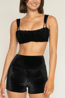 Woman wearing black velvet micro shorts with high waistband and matching ruched crop top with thin straps.