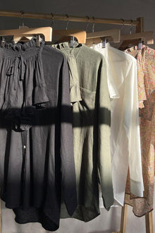 Black linen shorts with drawstring waist and gathered fabric detail, displayed on wooden hanger.