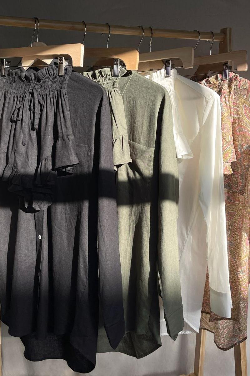 Black linen shorts with drawstring waist and gathered fabric detail, displayed on wooden hanger.