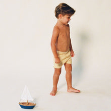Child wearing yellow and white striped swim trunks, standing in profile against a neutral background.