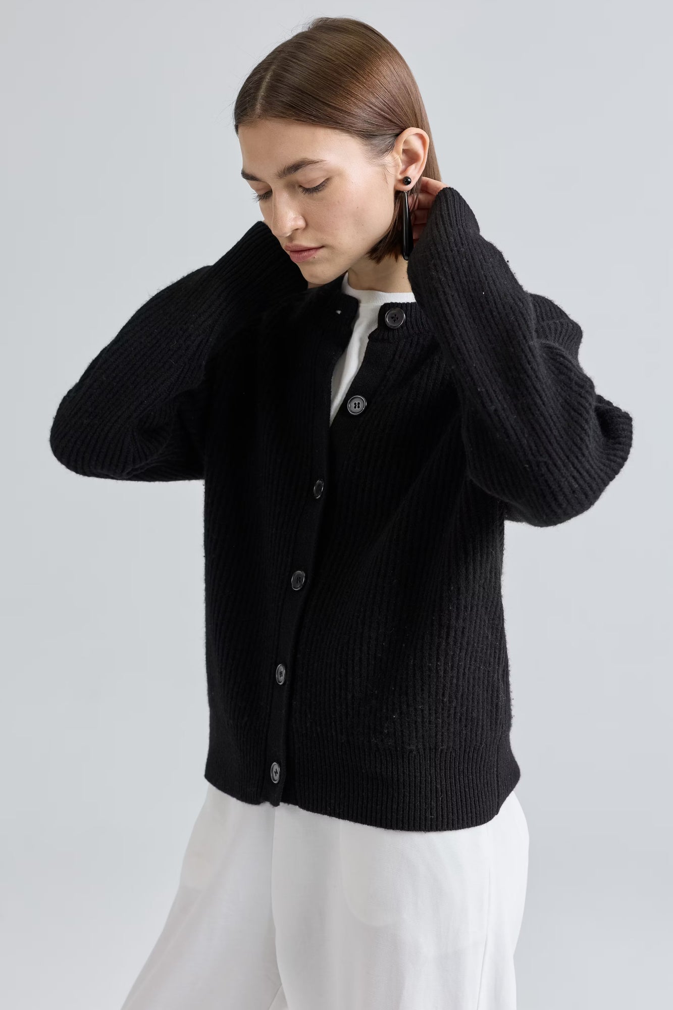 Woman wearing a black cardigan over a white shirt on a light gray background