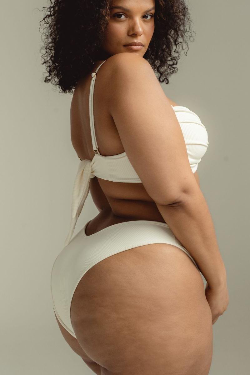 Cream ribbed bikini bottom with tie-back closure shown on model from rear view.
