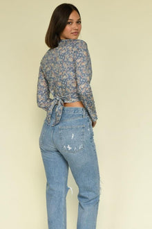 Blue paisley wrap top with long sleeves tied at back, worn with distressed light wash jeans.