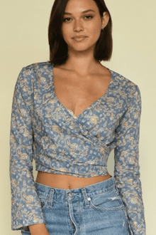 Woman wearing a blue wrap top with tan floral print and long sleeves paired with light blue denim jeans.